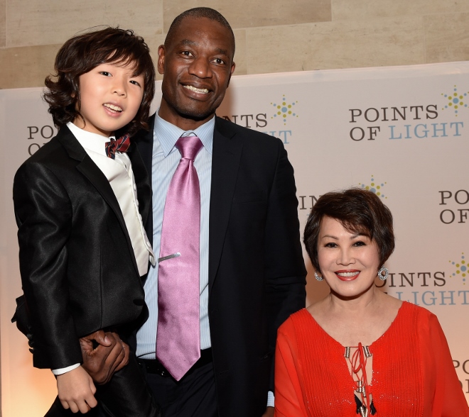 Basketball great Dikembe Mutombo lifts up prodigy cellist Justin Yu as honorary co-chair Yue-Sai Kan is amused by the heights.