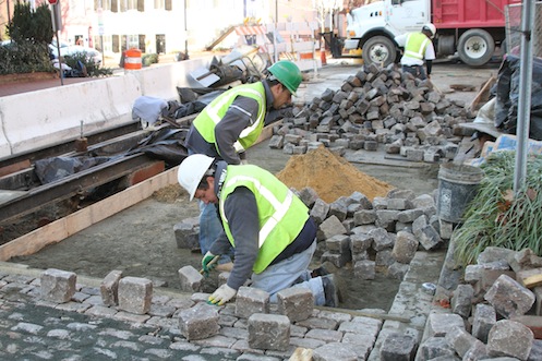 Workers position setts in a mixture of sand and dry cement, then finish with a blue stone dust.