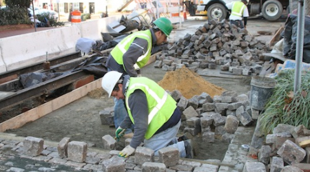 Workers position setts in a mixture of sand and dry cement, then finish with a blue stone dust.
